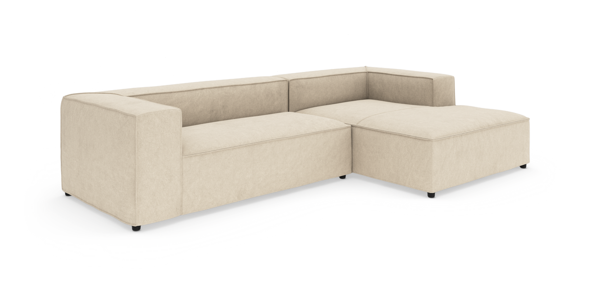 Beige L-formet modulsofa med bred chaiselong, lav ryg og blokarmstøtter på hvid baggrund.