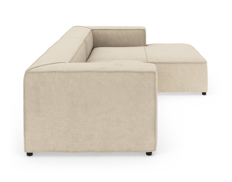 Beige modulsofa i L-form med brede armlæn, set fra siden på hvid baggrund.