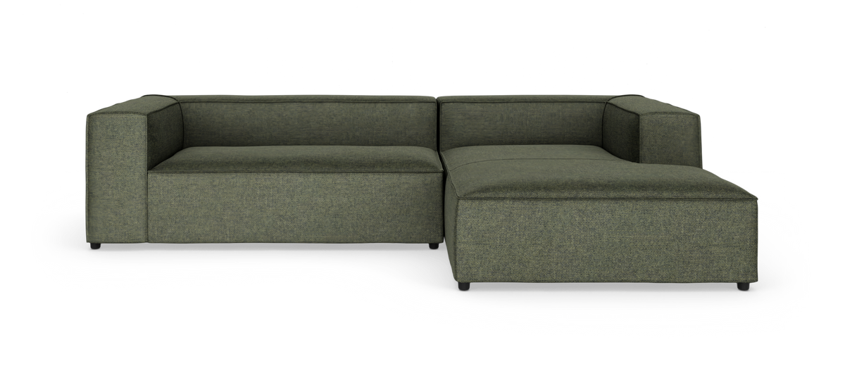 Grøn modulsofa i L‑form med chaiselong til højre, fotograferet mod hvid baggrund.