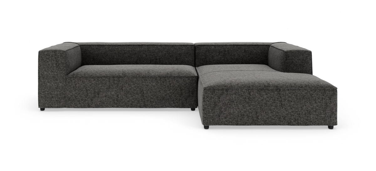 Mørkegrå modulsofa med chaiselong i højre side, fotograferet forfra i studie på hvid baggrund.