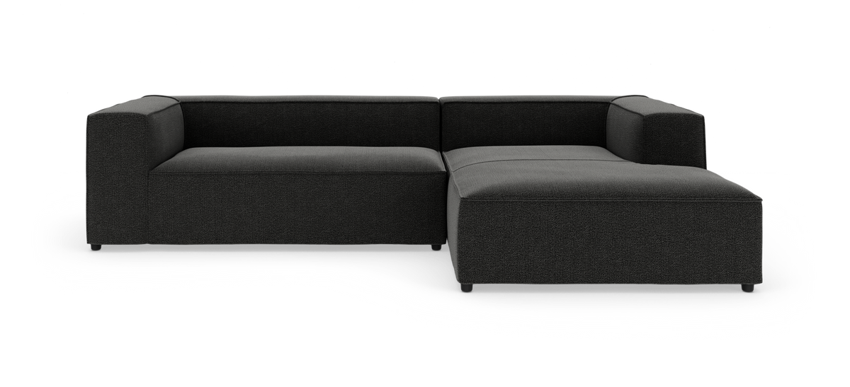 Mørkegrå modulsofa i L‑form med chaiselong til højre på hvid baggrund.