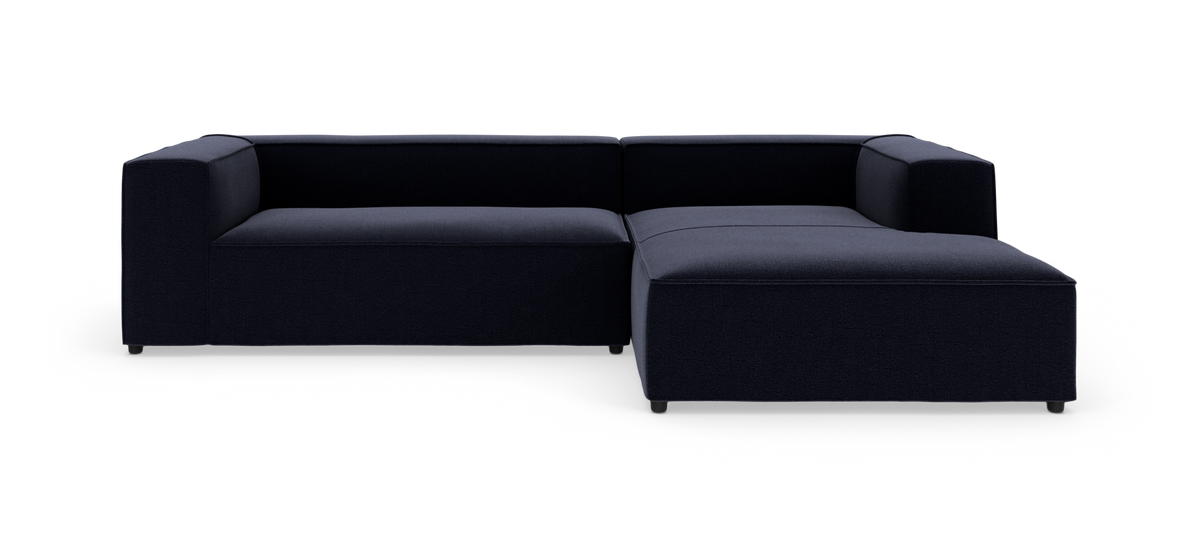Mørkeblå L-formet modulsofa med chaiselong til højre på hvid baggrund.