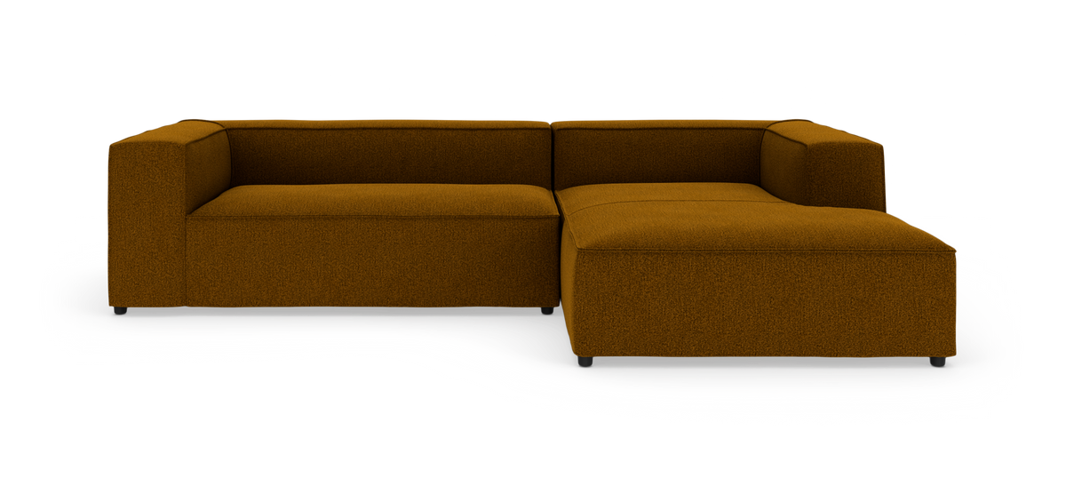Modulær L-formet sofa i sennepsgul/brun tekstil med brede armlæn og højrevendt chaiselong, frilagt på hvid baggrund.