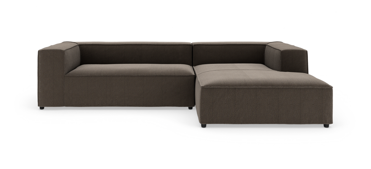 Brun L-formet modulsofa i stof på hvid frilægning, med brede armlæn og lav sæde.