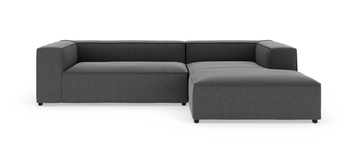 Mørkegrå modulsofa i L‑form med chaiselong til højre, frontvisning på hvid studiobaggrund.