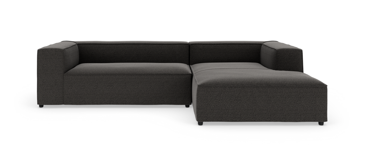 Mørkegrå L-formet modulsofa med chaiselong til højre på hvid baggrund.