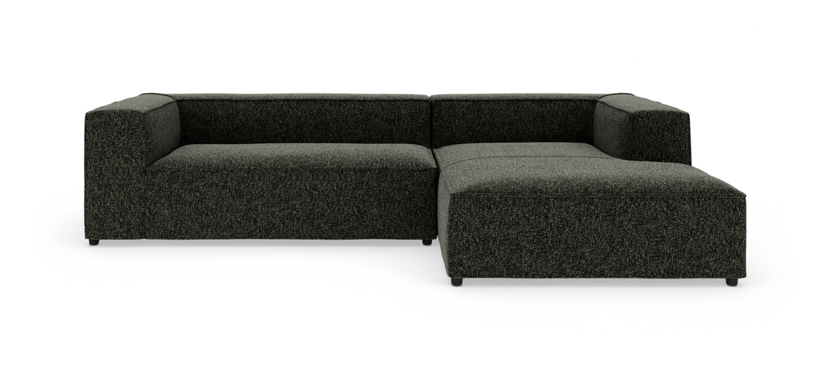 Mørkegrå modulsofa med chaiselong til højre, fotograferet mod hvid studiobaggrund.