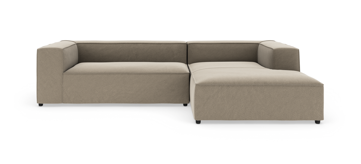 Beige L-formet modulsofa med brede blokarmlæn og højrevendt chaiselong, fotograferet mod hvid baggrund.