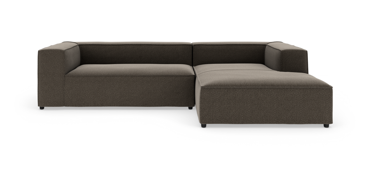 Modulsofa i L-form med chaiselong til højre i mørkegråt stof på hvid baggrund.