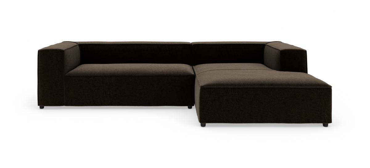 Mørkebrun modulsofa i L‑form med chaiselong til højre på hvid baggrund.