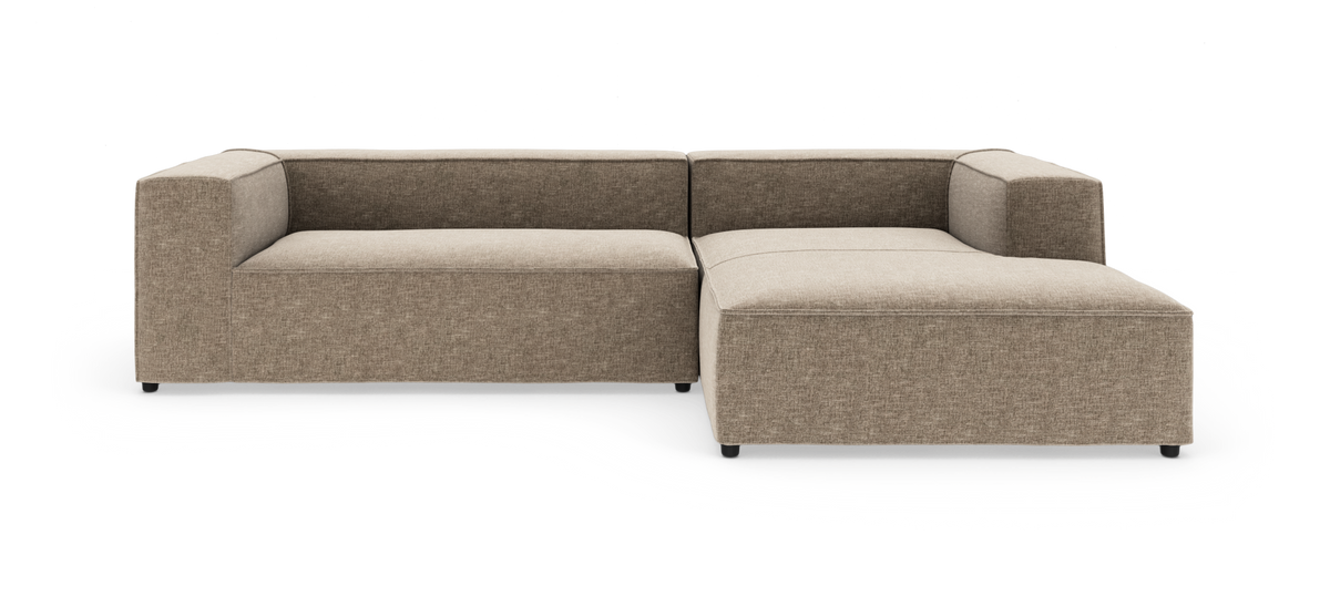 Modulsofa i L-form med brede armlæn og højre chaiselong i beige stof, frilagt på hvid baggrund.