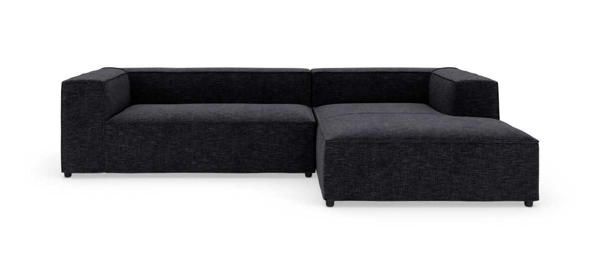 Mørkegrå L‑formet modulsofa fotograferet i studie mod hvid baggrund.