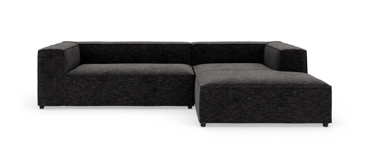 Mørkegrå modulsofa i L‑form med chaiselong til højre, frilagt på hvid baggrund.