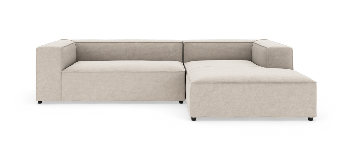 Modulsofa i beige stof med højre chaiselong, kubeformede armlæn og lav profil, frilagt på hvid baggrund.