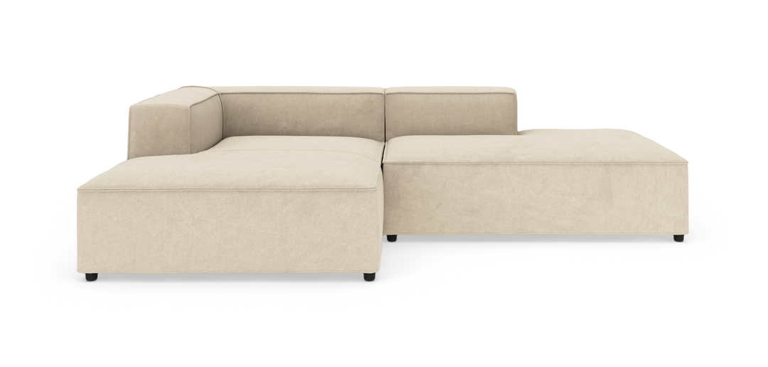 Beige modulsofa i L‑form med brede sæder, lav ryg og sorte ben, frilagt på hvid baggrund.