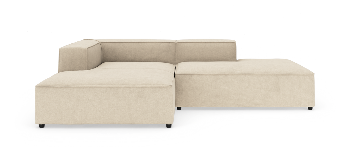 Beige modulsofa i L‑form med brede sæder, lav ryg og sorte ben, frilagt på hvid baggrund.