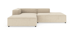 Beige modulsofa i L‑form med brede sæder, lav ryg og sorte ben, frilagt på hvid baggrund.