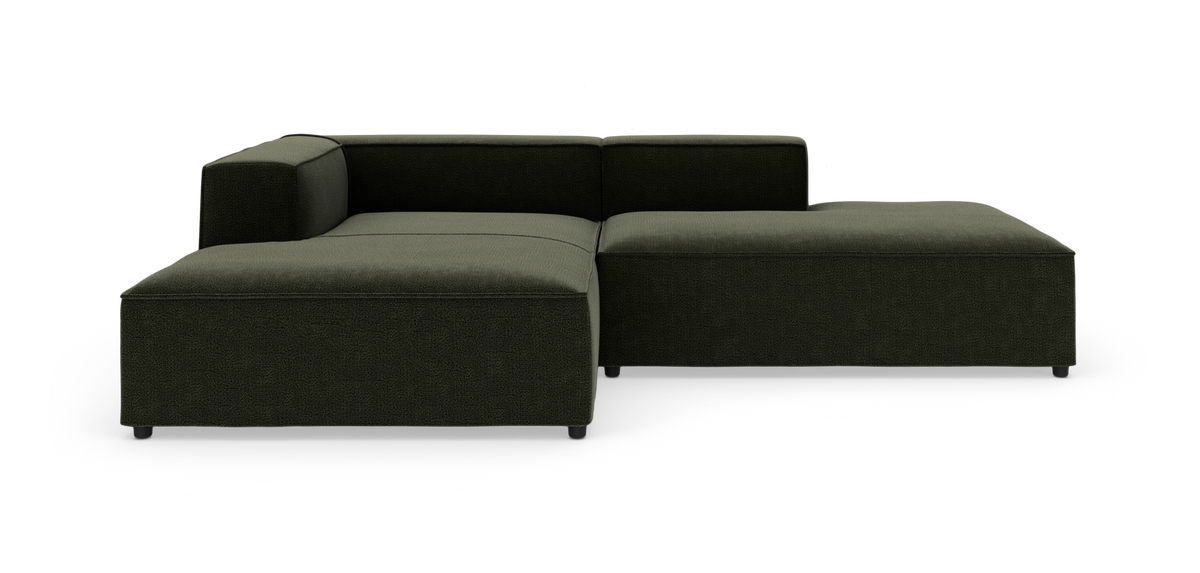 Mørkegrøn modulsofa i L‑form med lav ryg og bred chaiselong til højre, frilagt mod hvid baggrund.