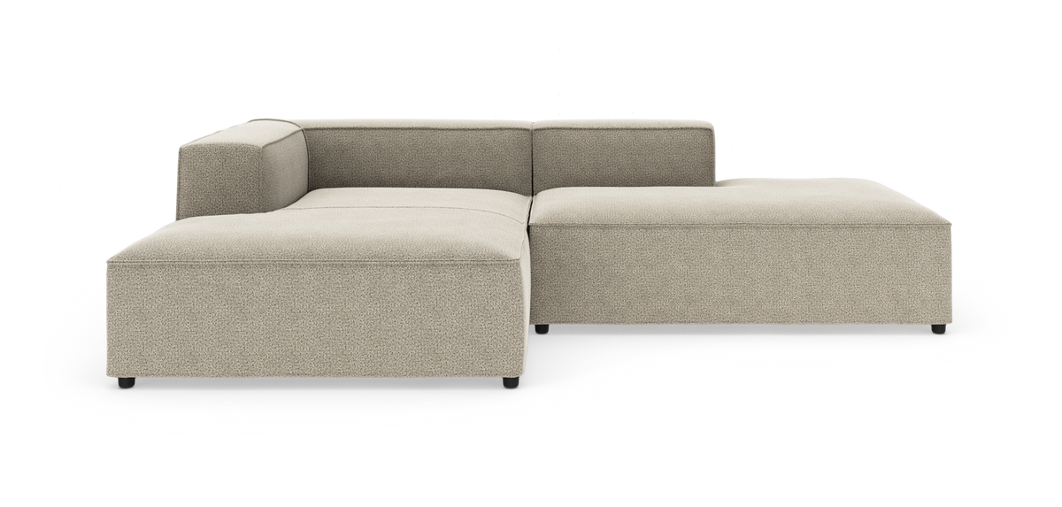 Beige modulsofa i L-form med lav ryg og bløde, blokagtige former på hvid studiebaggrund.