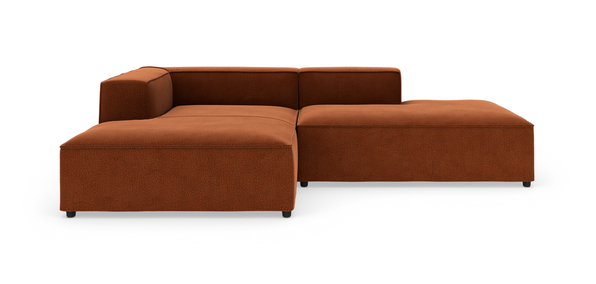 Modulær L‑sofa i rustfarvet tekstil med lav ryg og brede sæder, frilagt på hvid baggrund.