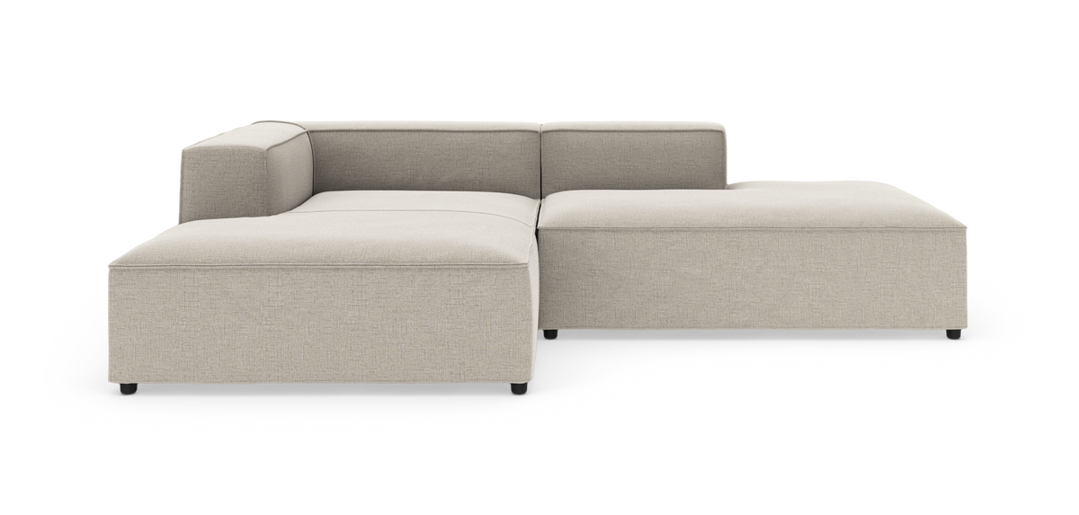 Beige L‑formet modulsofa med lav ryg og bred chaiselong, fritlagt på hvid baggrund.