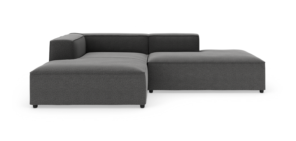 Mørkegrå modulsofa i L‑form med lav ryg og brede sædehynder, fotograferet i studie på hvid baggrund.