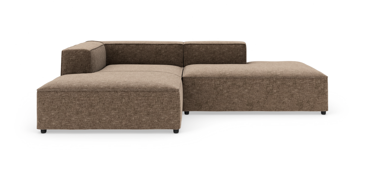 Modulær hjørnesofa i brun/beige stof med lav ryg og brede sædehynder på hvid frilagt baggrund.