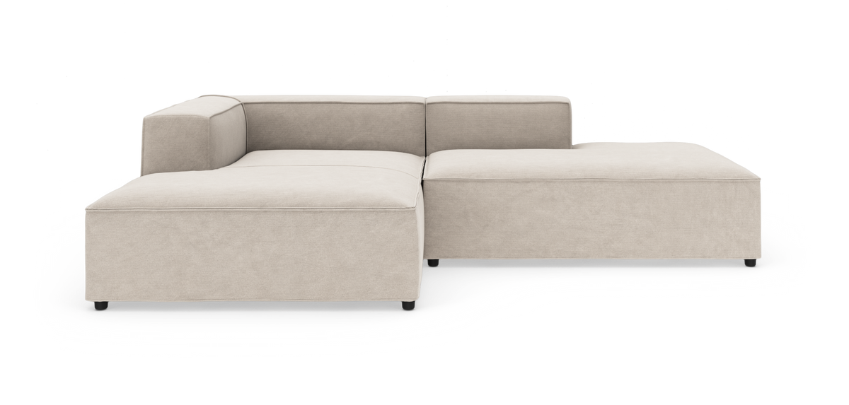 Beige modulsofa i L‑form med lav ryg og bred chaiselong, vist på hvid baggrund.