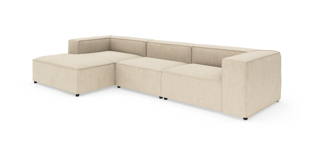 Beige modulsofa i L‑form med venstrevendt chaiselong, lav ryg og brede armlæn, frilagt på hvid baggrund.
