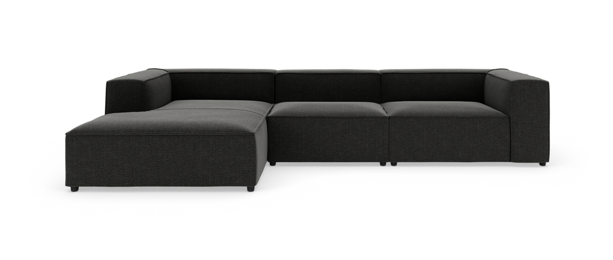 Modulær hjørnesofa med chaiselong i mørkegråt stof, vist i studie på hvid baggrund.