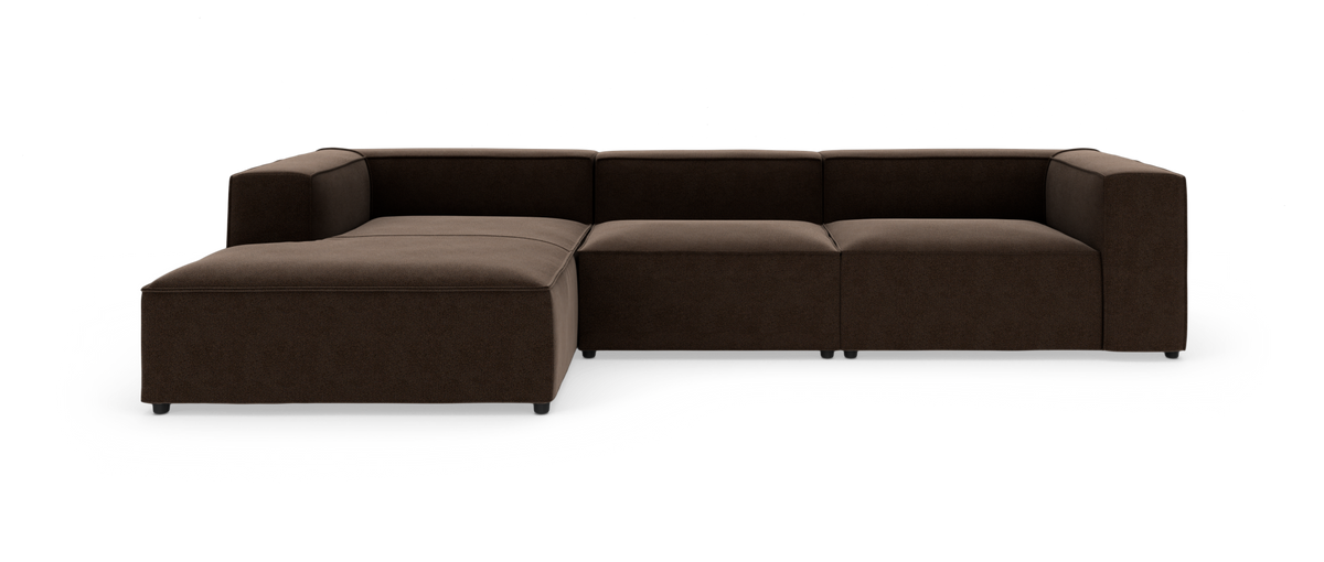 Modulsofa i mørkebrun tekstil med venstre chaiselong, lav profil og brede armlæn, frilagt på hvid baggrund.