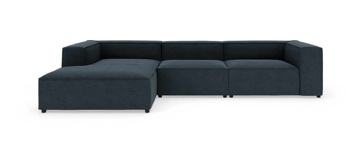 Mørkeblå modulsofa i L-form med chaiselong til venstre på hvid baggrund.