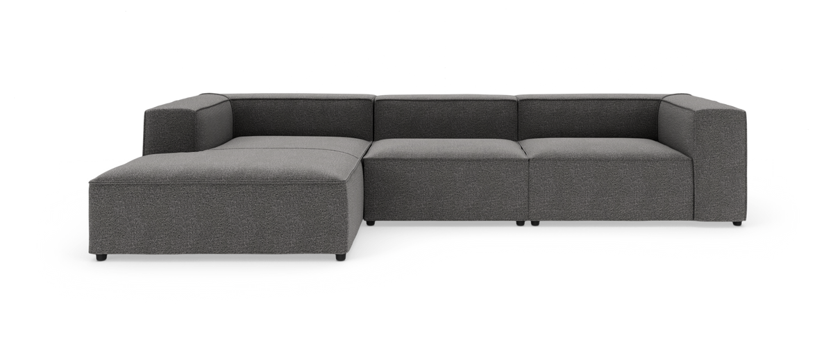 Mørkegrå modulsofa med venstrevendt chaiselong, kraftige kubeformede armlæn og lav profil, frilagt på hvid baggrund.