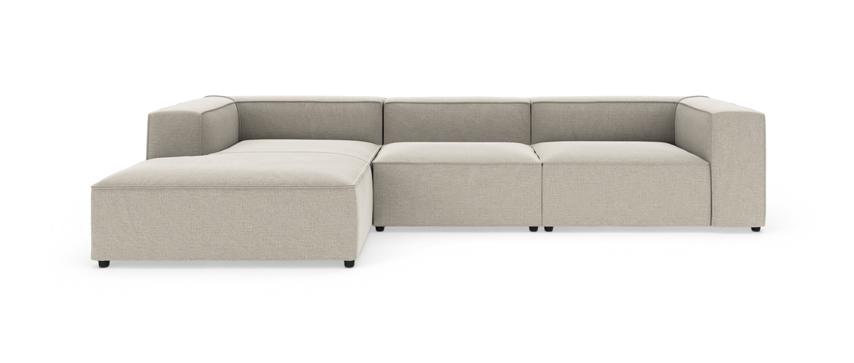 Beige modulsofa med venstrevendt chaiselong og brede, firkantede armlæn, set forfra på hvid baggrund.