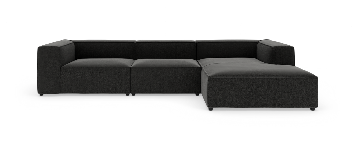 Modulær hjørnesofa i mørkegråt/sort stof med chaiselong til højre, frilagt på hvid baggrund.