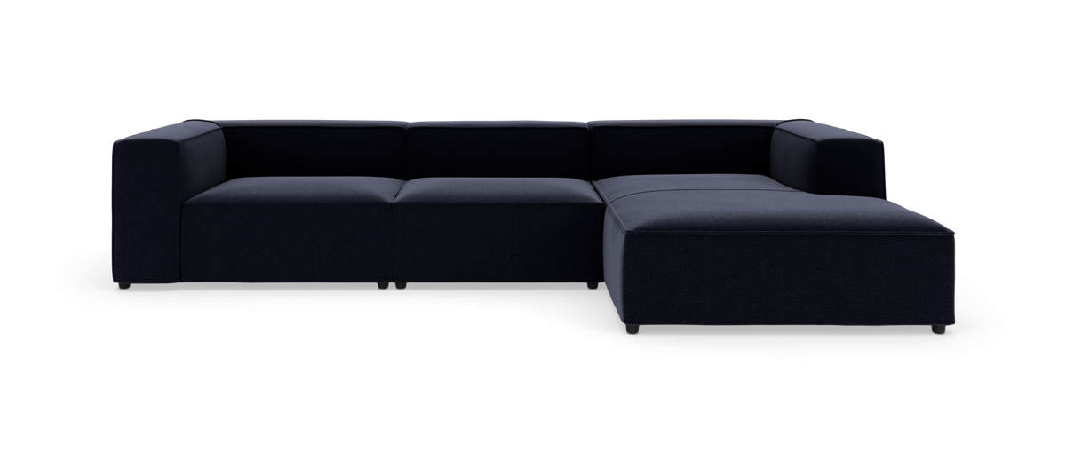 Mørkeblå modulsofa med chaiselong til højre på hvid baggrund.