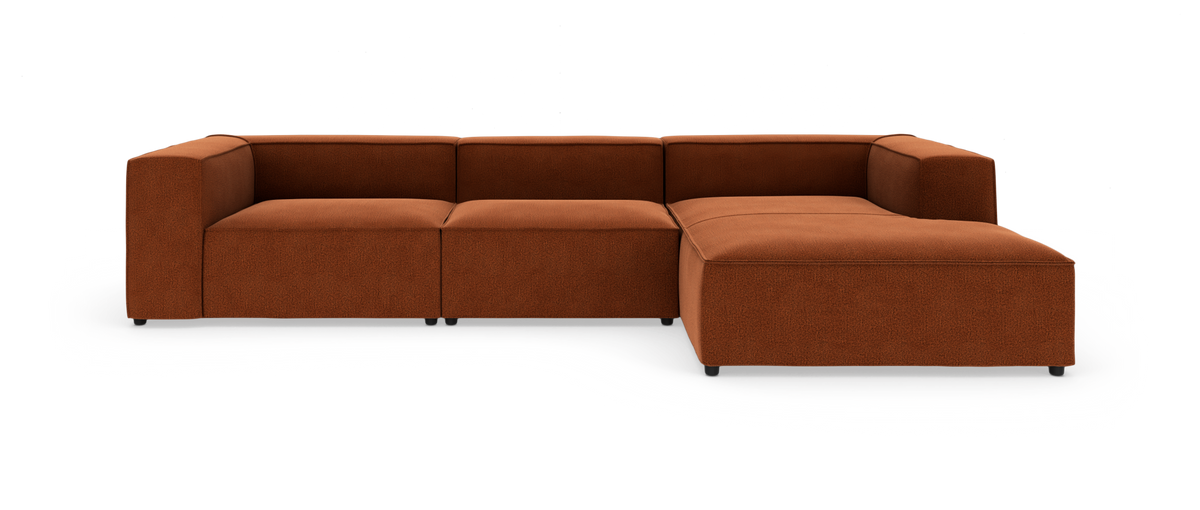 Modulsofa i terrakottafarvet tekstil med chaise longue til højre og kubiske armlæn, fritlagt på hvid baggrund.