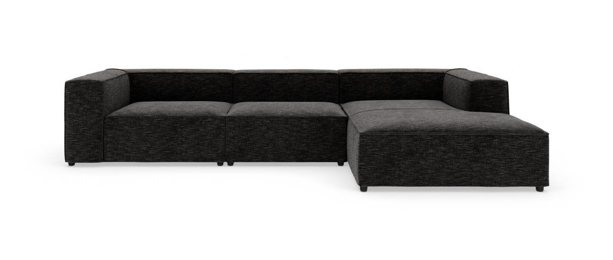 Mørkgrå modulsofa i L-form, lav og dyb med brede armlæn, frilagt på hvid baggrund.