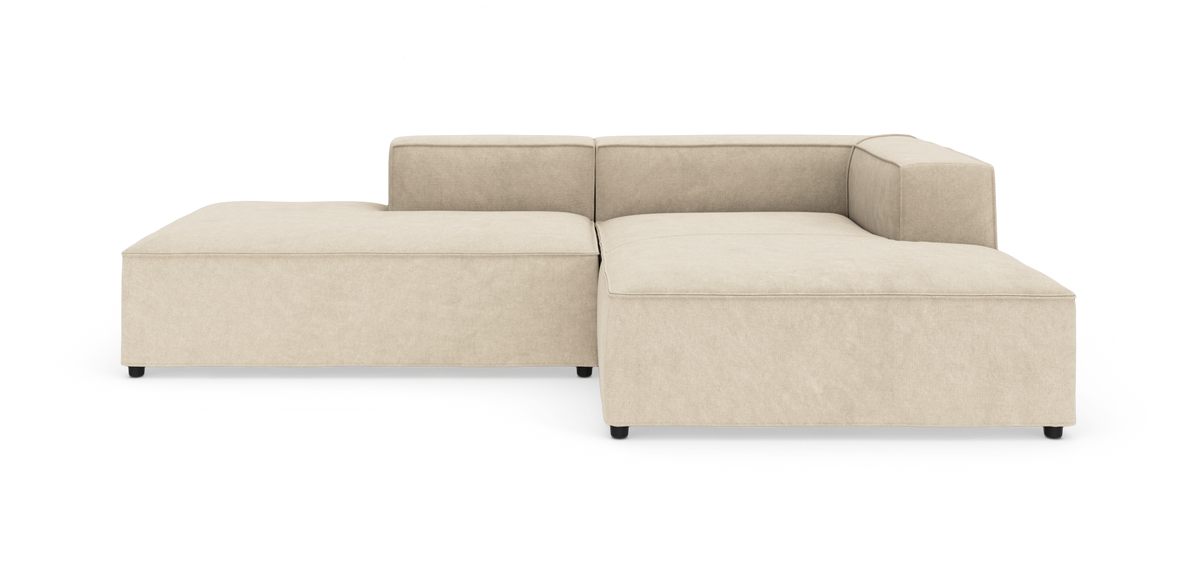 Beige modulsofa i L‑form med brede armlæn og lav profil på hvid baggrund.