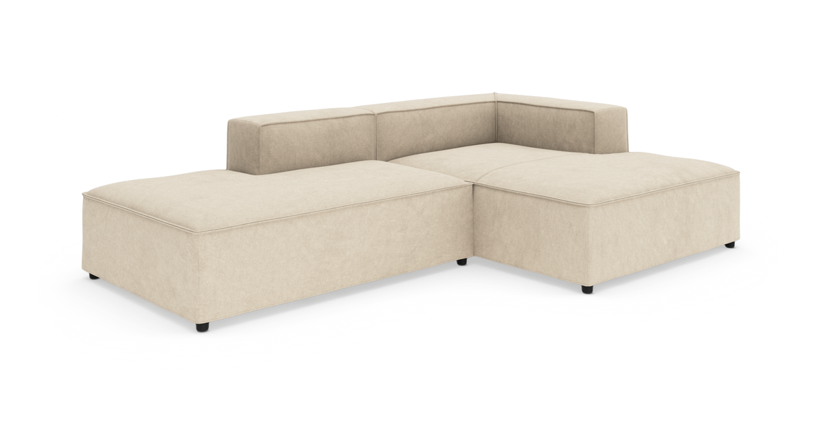 Beige modulsofa i L-form på hvid baggrund med lav ryg og brede sædehynder.