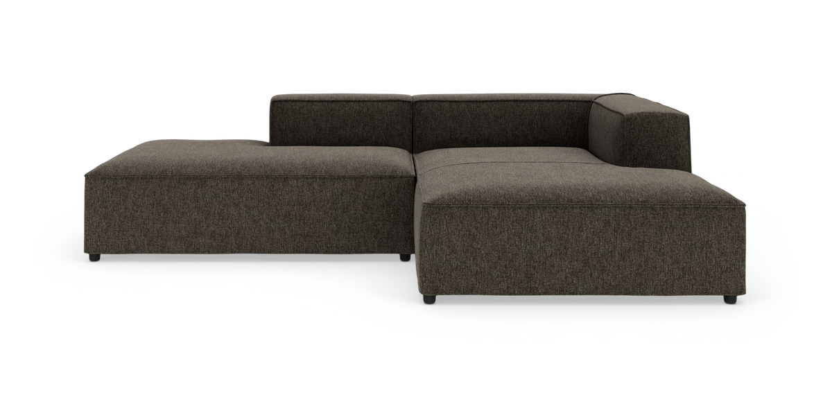 Mørkegrå L‑formet modulsofa med lav ryg på hvid baggrund.