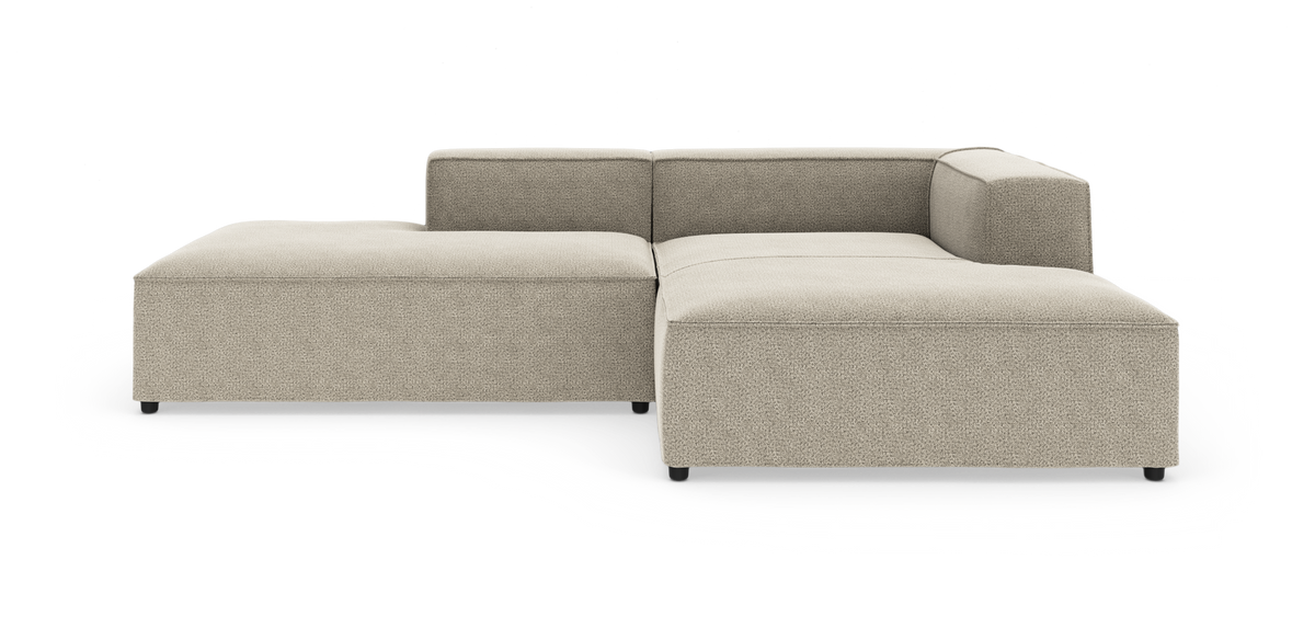 Beige modulsofa i L‑form med lav ryg og bred chaiselong, vist på hvid studiebaggrund.