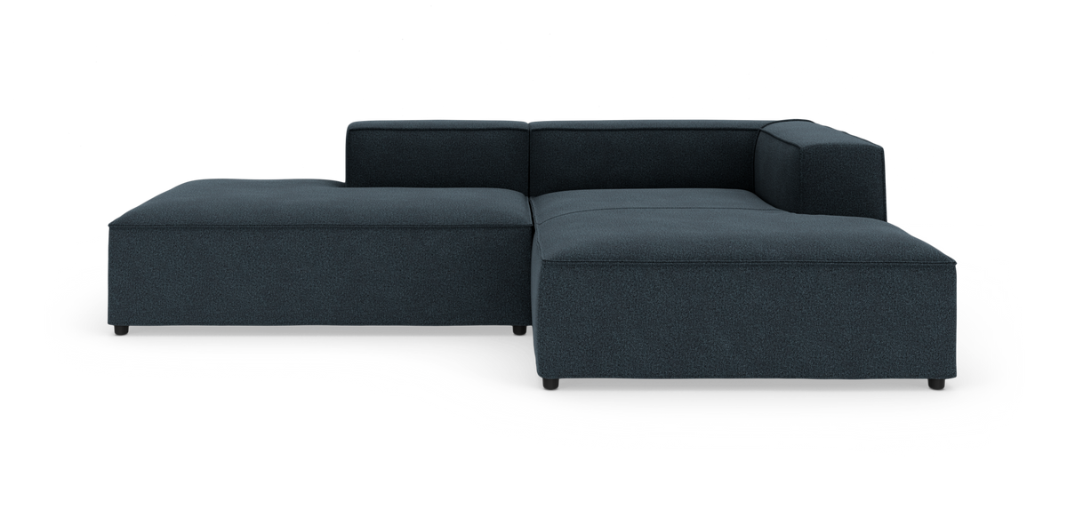 Mørkeblå L‑formet modulsofa med lav ryg og bred chaiselong på hvid baggrund.