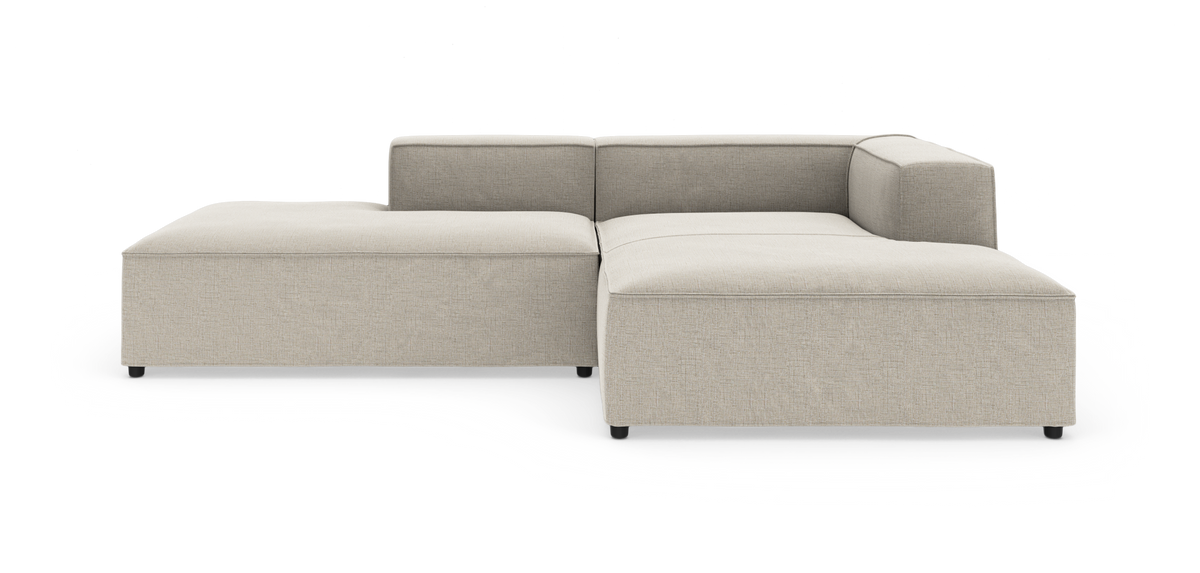 Beige L‑formet modulsofa med lav ryg og brede armlæn, frilagt på hvid baggrund.