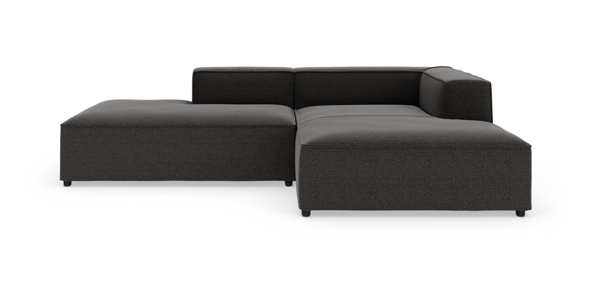 Mørkegrå modulsofa i L‑form med chaiselong, vist på studiebaggrund fra let skrå frontvinkel.