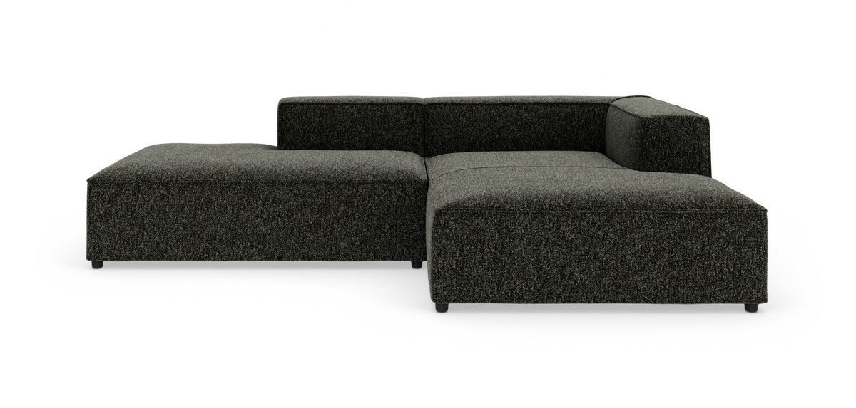 Mørkegrå modulsofa i L‑form med lav ryg og bløde, afrundede kanter, fritstående på hvid baggrund.
