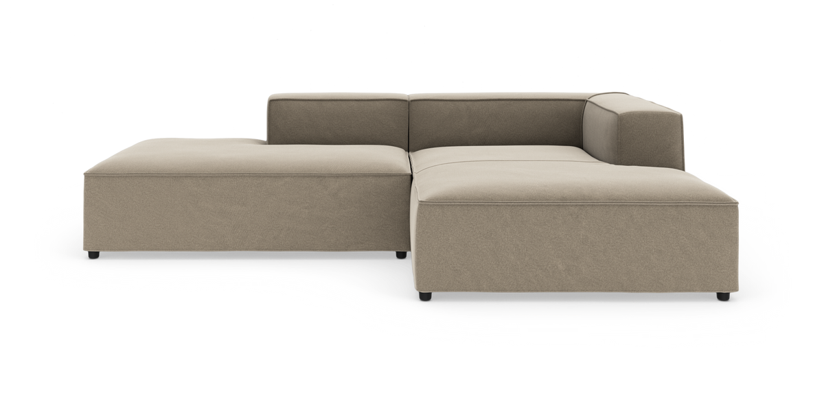 Modulsofa i L-form i beige stof på hvid baggrund med lav ryg og bred chaiselong til venstre.