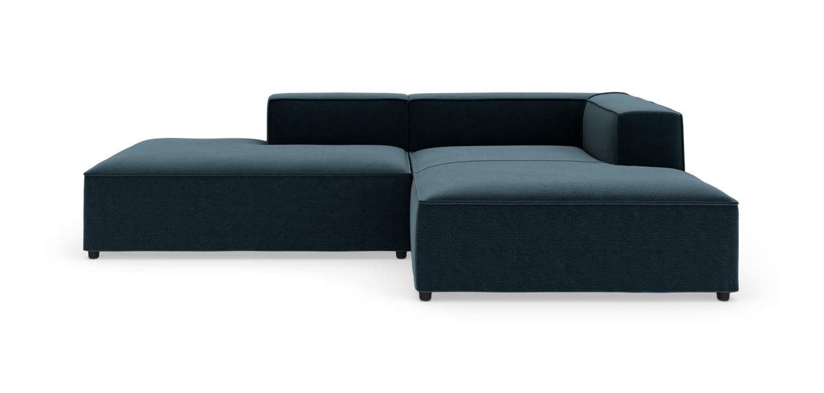 Modulsofa i mørk blågrøn tekstil med venstrevendt chaiselong, lav ryg og højre armlæn, fotograferet på hvid studiobaggrund.