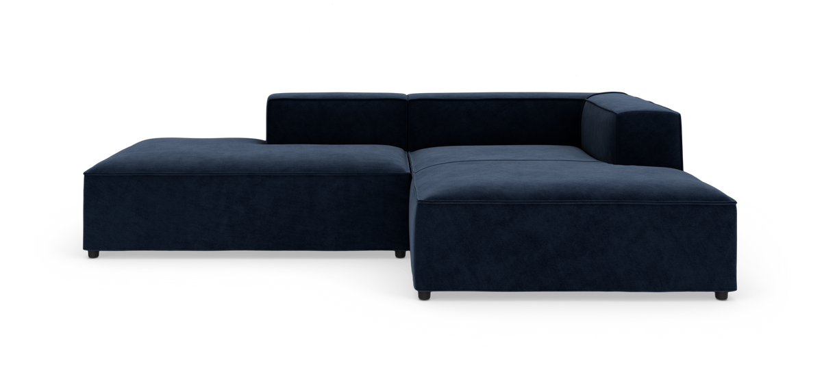Mørkeblå modulsofa i L‑form med lav ryg og bred chaiselong, frilagt på hvid baggrund.