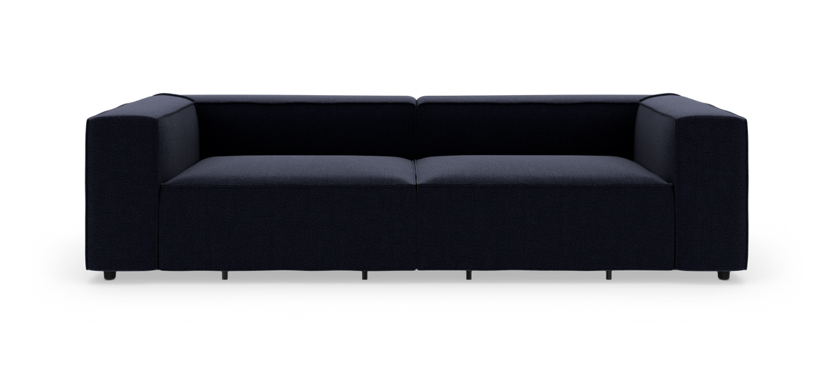 Mørkeblå, moderne modulsofa med brede armlæn set forfra mod hvid studiobaggrund.
